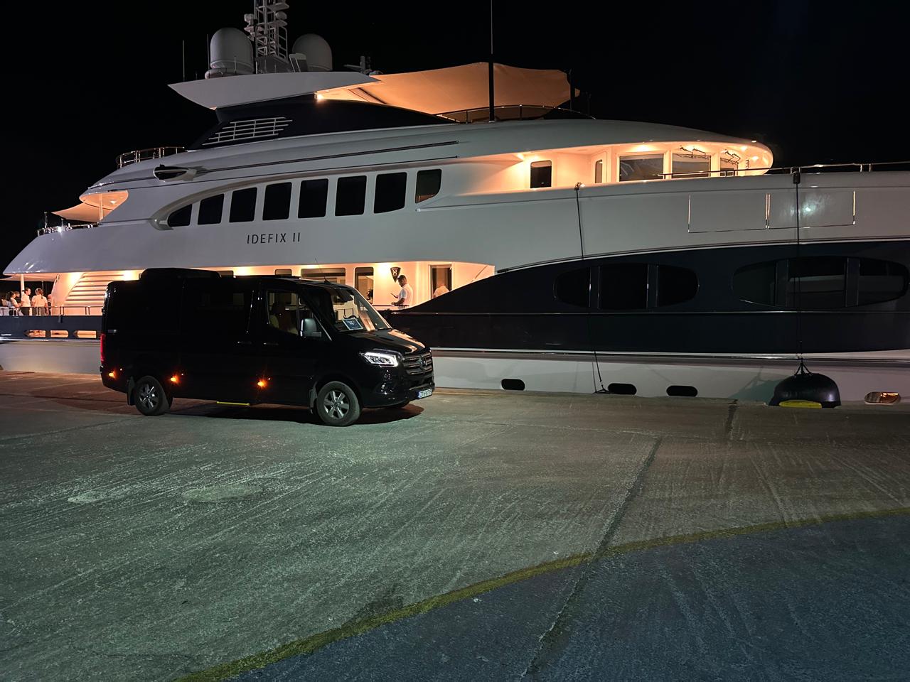 Black luxury Mercedes-Benz chauffeur van parked at an illuminated superyacht marina pier during an evening half-day tour
